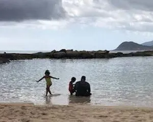 A man and two children sitting in the water at the beach.