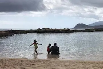 A man and two children sitting in the water at the beach.