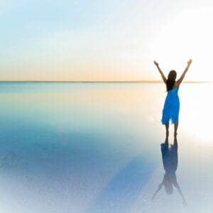 A woman standing on the beach with her arms in the air.