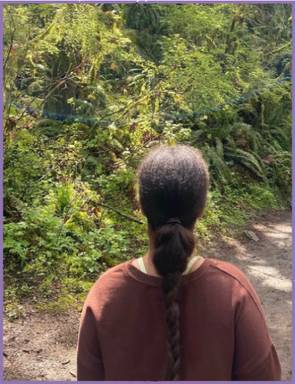 A woman with long hair is standing in front of some bushes.