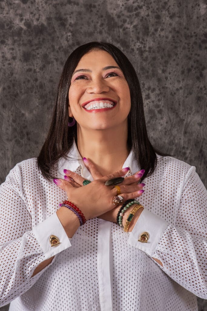 A woman smiling and holding her hands in front of her chest.